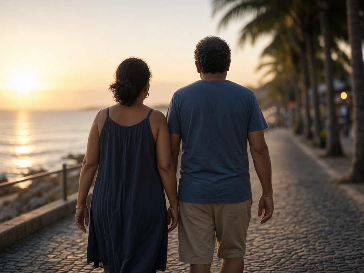 Casal de meia-idade de costas caminhando lado a lado num calçadão à beira-mar ao pôr do sol