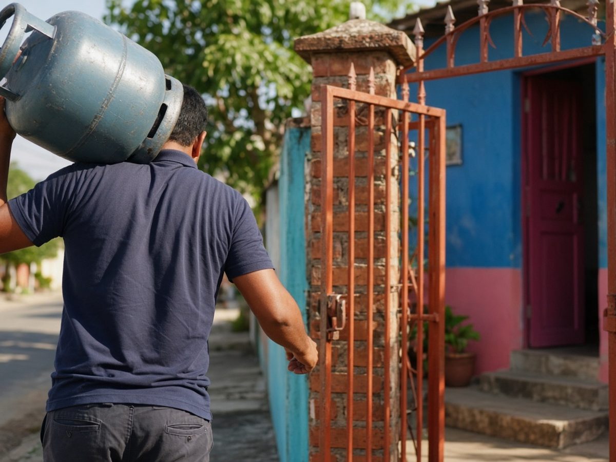 Entregador de costas carregando um botijão de gás no ombro até o portão de uma casa