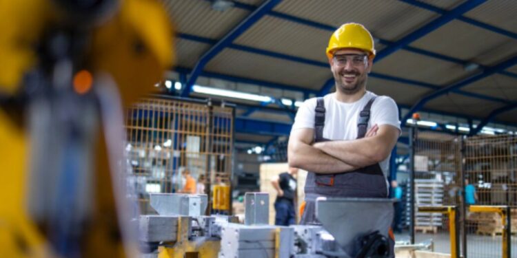 Pessoa sorridente e de braços cruzados em uma fábrica